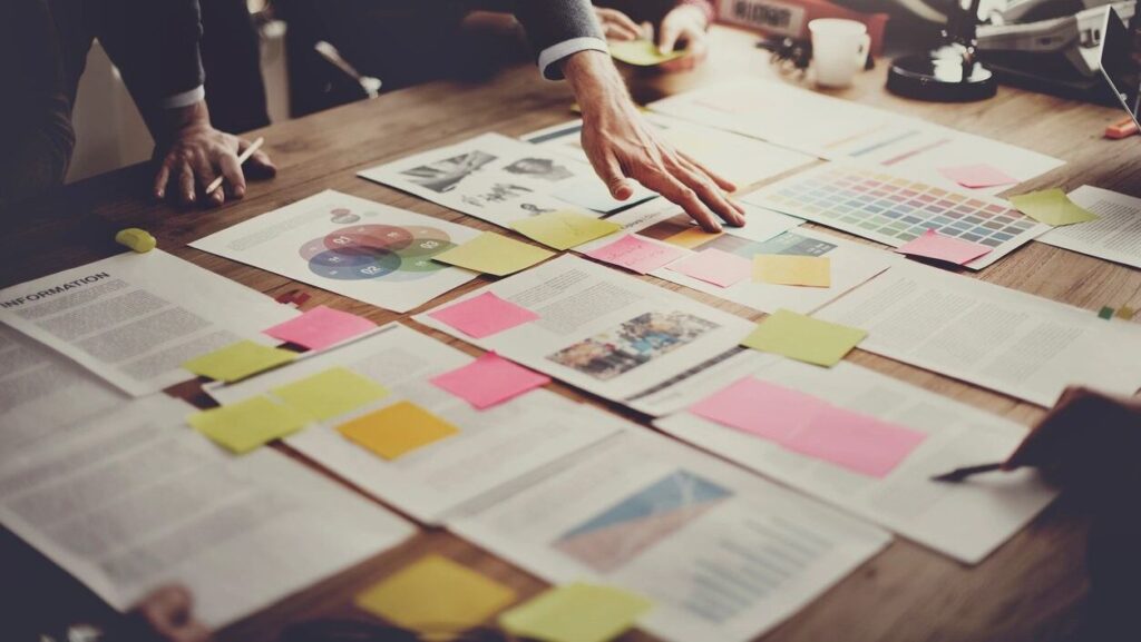 Table with hands shuffling papers and sticky notes.